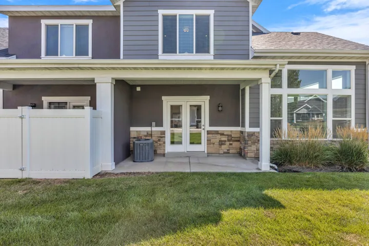 Modern two-story home featuring a covered front porch with white columns and stone accents, French doors with multi-pane glazing, and a welcoming entry