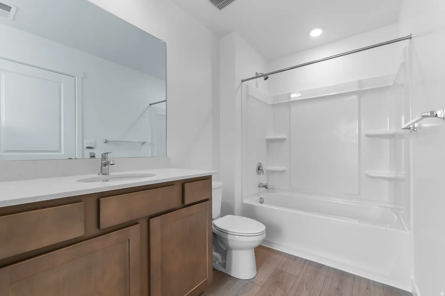 Bathroom featuring a wood-finish vanity with a single sink and light-toned countertop, a full-width mirror, and a white tub/shower combination with integrated shelving