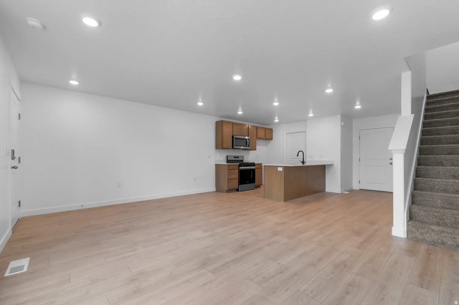 Open-concept living area featuring light wood-finish flooring, recessed lighting, and a modern kitchen