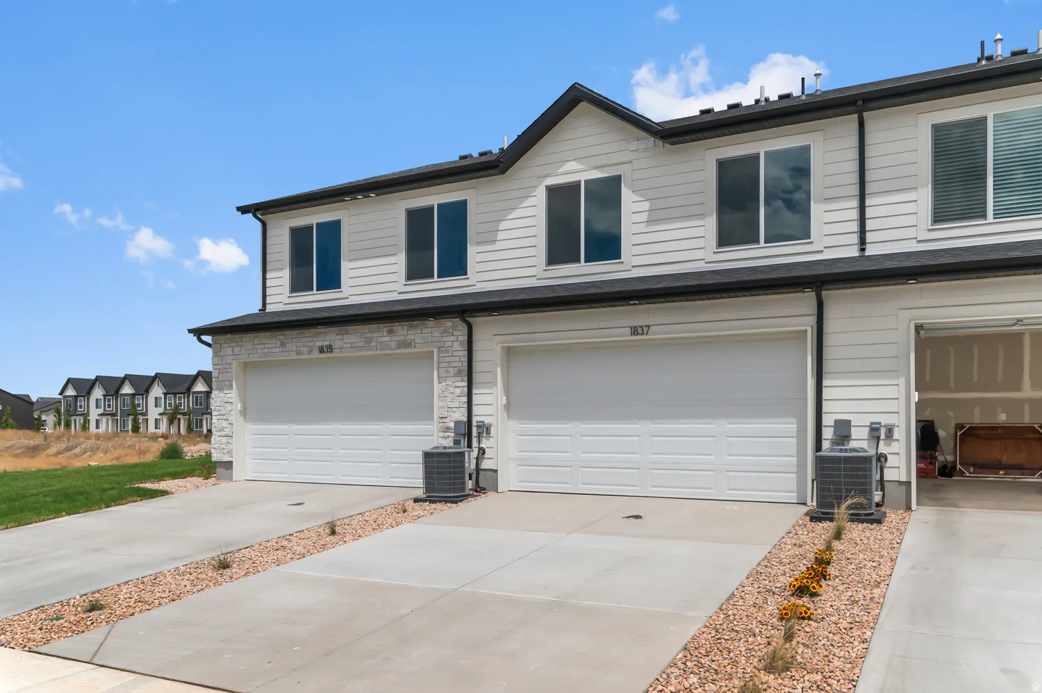 Contemporary townhome exterior featuring light-colored siding, a stone facade accent, and black-trimmed windows