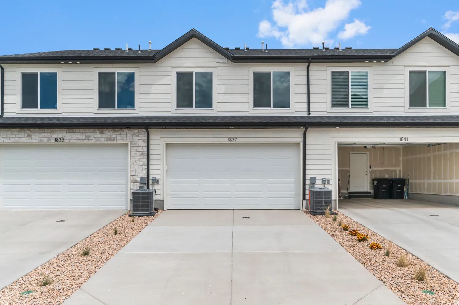 Townhome exterior featuring white siding, dark shingle roof, and stone accents