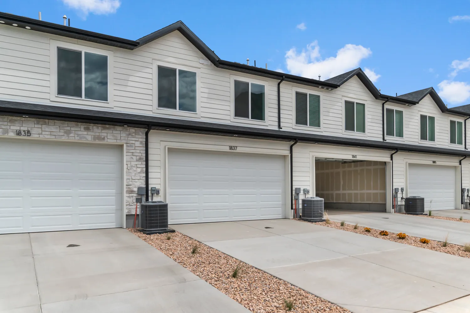 Modern townhome-style residence featuring a clean-lined facade with light gray fiber cement siding, multiple large multi-pane windows, and a peaked roofline with dark architectural shingles