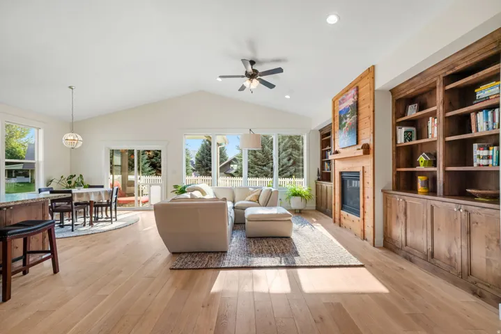 Vaulted ceiling living area featuring light wood-finish flooring, a built-in fireplace with wood surround, extensive built-in wooden shelving, and large windows