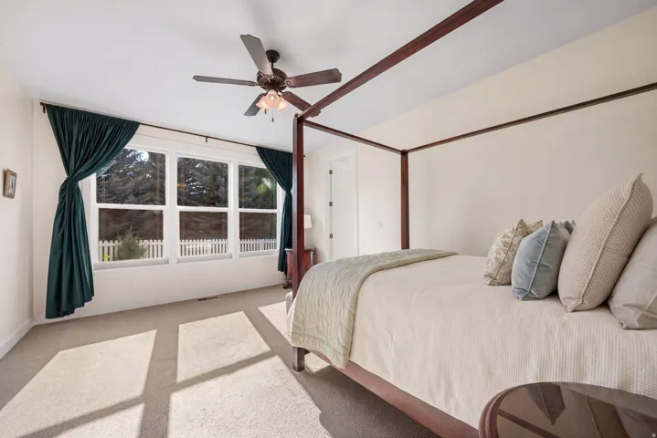 Luxurious primary bedroom suite featuring a four-poster wood bed frame, ceiling fan with integrated lighting, and abundant natural light from expansive glass doors opening to a private balcony with decorative railing
