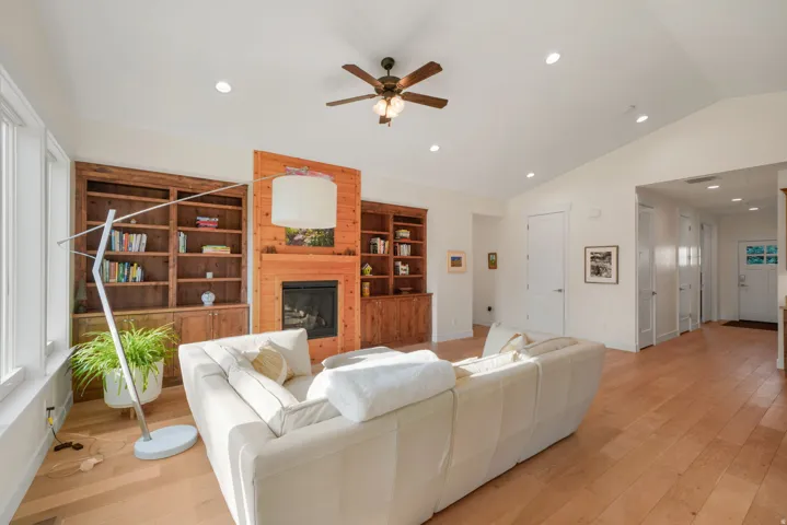 Spacious living room showcasing hardwood flooring, a custom wood-frame fireplace with built-in shelving, recessed ceiling lighting, and a ceiling fan