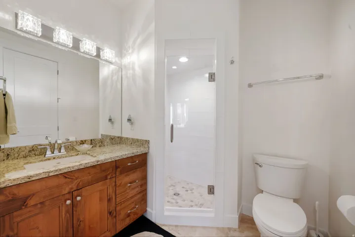 Full bathroom featuring a wood-finish vanity with a stone countertop, an undermount sink, and a mirrored wall