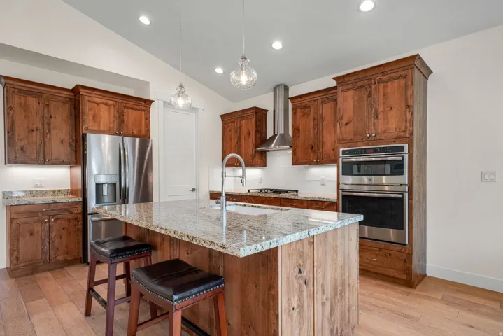 Gourmet kitchen featuring a large central island with a stone countertop, rich wood cabinetry, stainless steel appliances, a tile backsplash, and wood-finish flooring