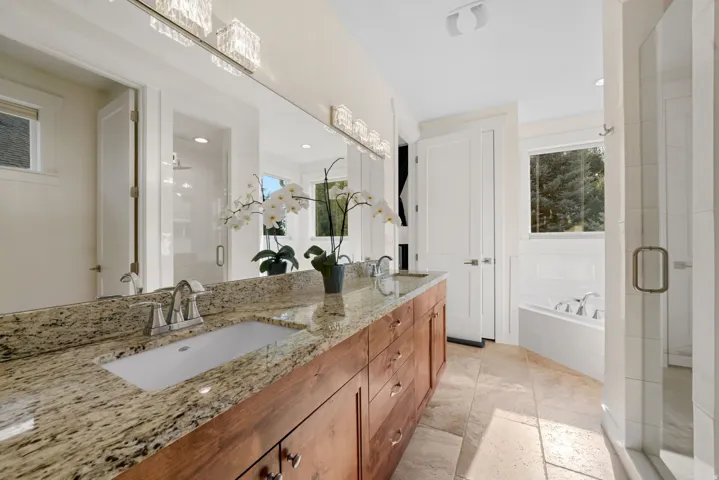 Spa-inspired primary bathroom featuring a dual-sink vanity with warm wood cabinetry, granite countertops, and brushed nickel hardware