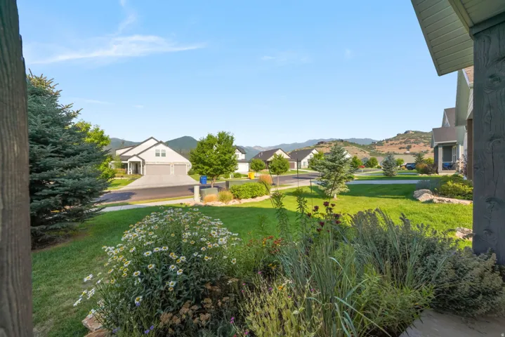Expansive grounds featuring manicured lawn, mature landscaping with flowering shrubs and ornamental grasses, and distant mountain backdrop