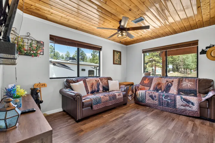 Bright and spacious living area showcasing wood plank ceiling with integrated ceiling fan, wood-finish flooring throughout, and abundant natural light from multiple large windows and glass doors