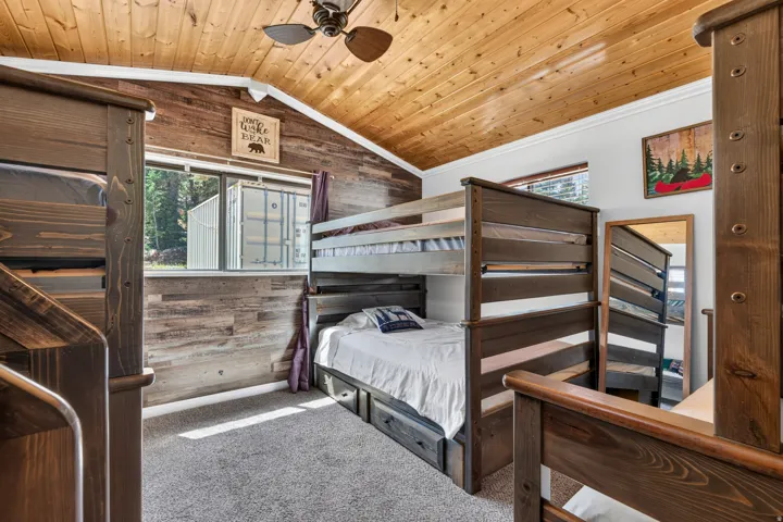 Vaulted wood-paneled ceiling with a ceiling fan, accent wall with horizontal wood planks, carpeted flooring, and a bunk bed with integrated storage drawers