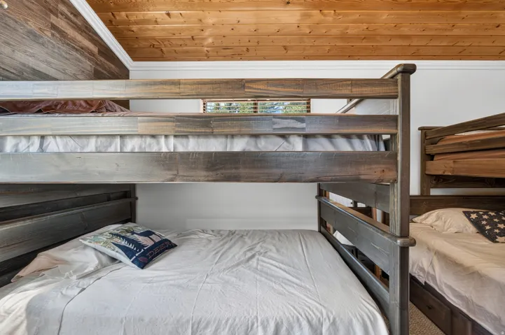 Bunk beds with distressed wood frames, wood-paneled accent wall, natural wood ceiling, crown molding, and a small window