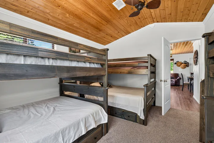 Spacious bedroom featuring dual bunk bed configurations with dark wood frames and white bedding, wood-plank cathedral ceiling with ceiling fan, carpeted flooring, and abundant natural light from windows
