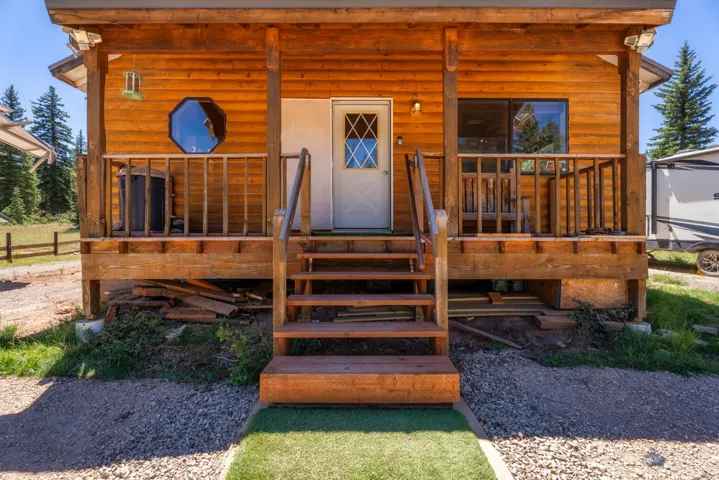 Charming log cabin exterior featuring a welcoming front porch with wooden railings, a centered entry door with decorative diamond-pane window, and a circular porthole accent window