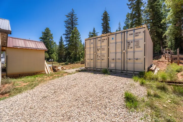 Spacious gravel parking area with two large storage containers, a separate utility building with a metal roof, and a wooden fence bordering the property