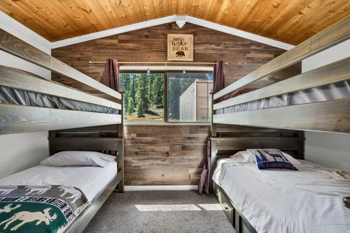 Cozy bedroom retreat featuring dual built-in twin beds with wood-finish frames, wood-paneled walls and ceiling, and a large window with natural light and outdoor scenery
