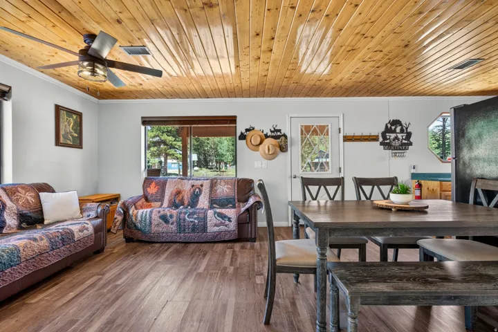 Open-concept living area with wood-finish flooring, a natural wood paneled ceiling, and a ceiling fan with integrated lighting