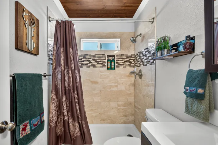 Tub and shower combination featuring a tiled surround, decorative mosaic accent band, and recessed niche