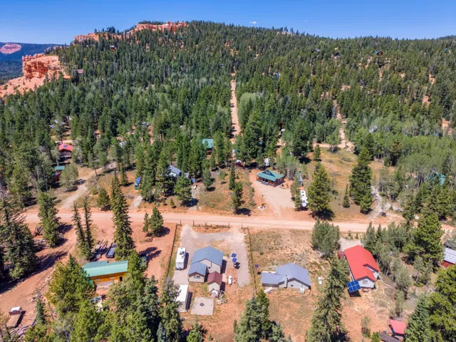 Aerial overview of a wooded property featuring multiple structures, unpaved roads, and a mountainous backdrop