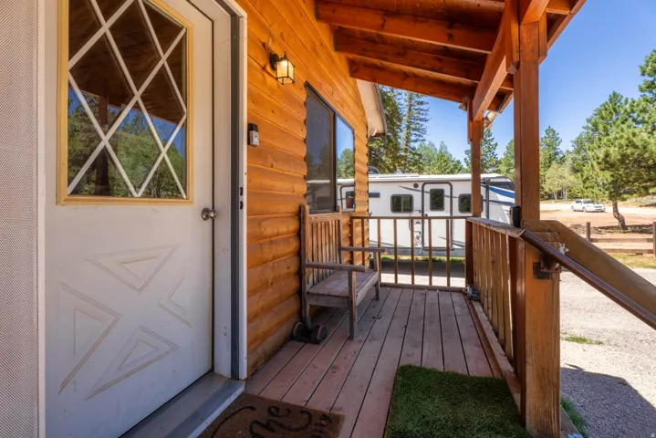 Inviting front porch featuring natural wood siding, exposed wood ceiling beams, and a white entrance door with decorative glass paneling