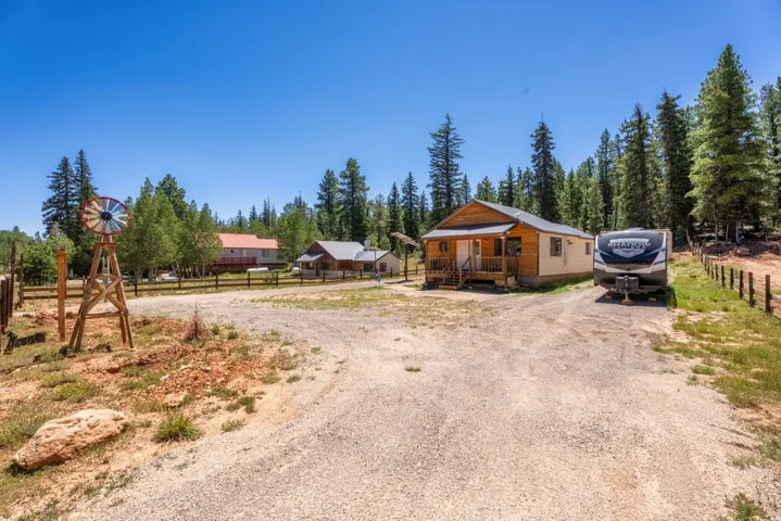 Gravel driveway with multiple structures, including a log-sided cabin featuring a covered porch with wood railings and steps