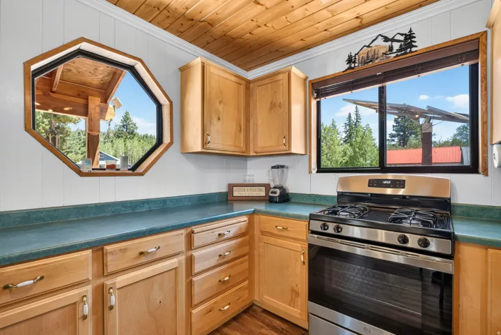 Kitchen featuring natural wood cabinetry, teal countertops, a stainless steel gas range, and a wood-paneled ceiling