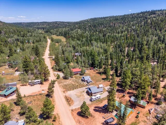Expansive aerial landscape featuring a dirt road winding through a forested setting with multiple residential structures