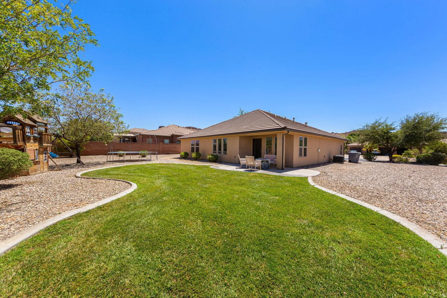 Expansive backyard featuring a manicured lawn, gravel landscaping, and a concrete patio