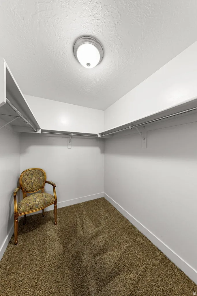 Walk-in closet featuring white walls, deep brown textured carpet, white baseboards, and built-in white wire shelving and hanging rods