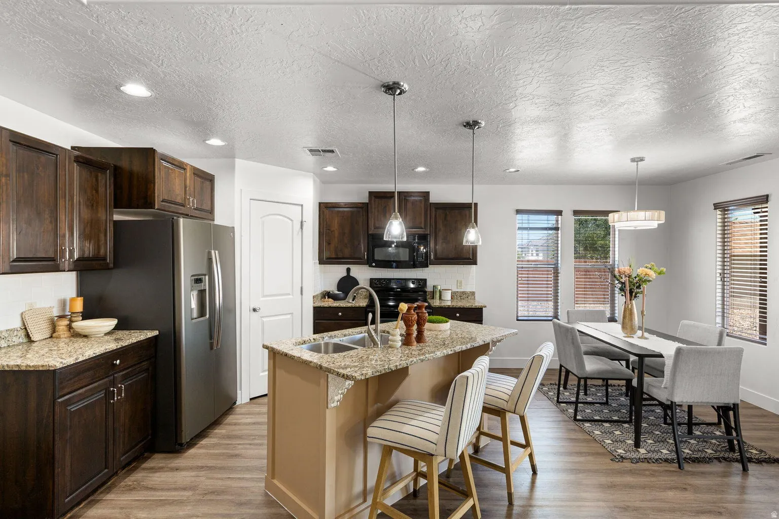 Open-concept kitchen and dining area featuring dark wood cabinetry, granite-finish countertops, stainless steel appliances, and wood-finish flooring