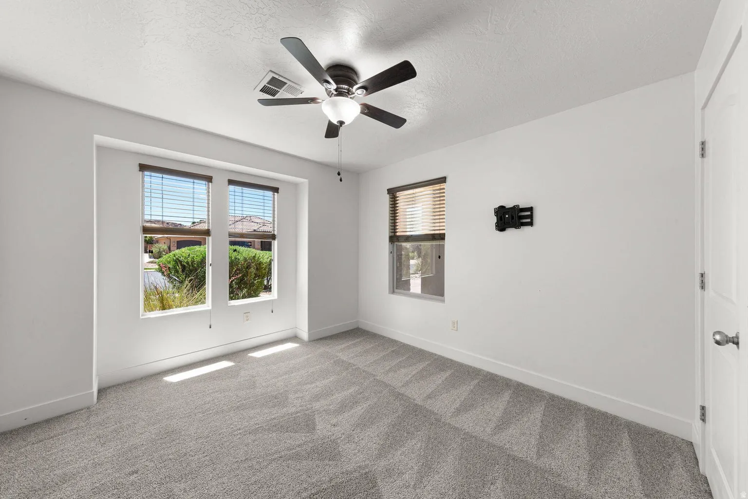 Bright interior space featuring light gray patterned carpeting, white walls, and a ceiling fan with integrated lighting