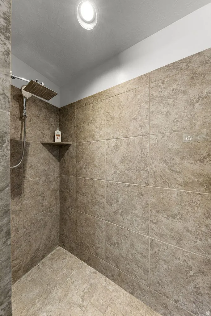 Walk-in shower with textured tile walls, coordinating tile flooring, a built-in corner shelf, and a ceiling-mounted rainfall showerhead