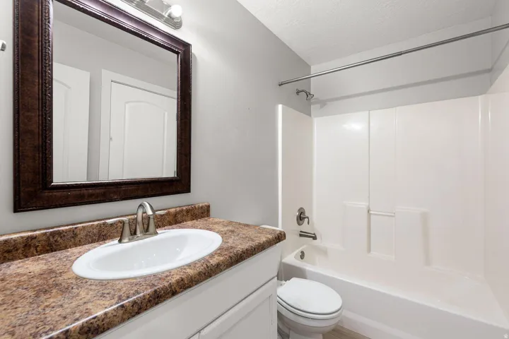 Bathroom vanity with a decorative framed mirror, integrated sink, and granite-finish countertop