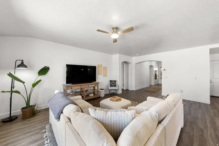 Spacious living area featuring wood-finish flooring, a ceiling fan with integrated lighting, and multiple arched doorways