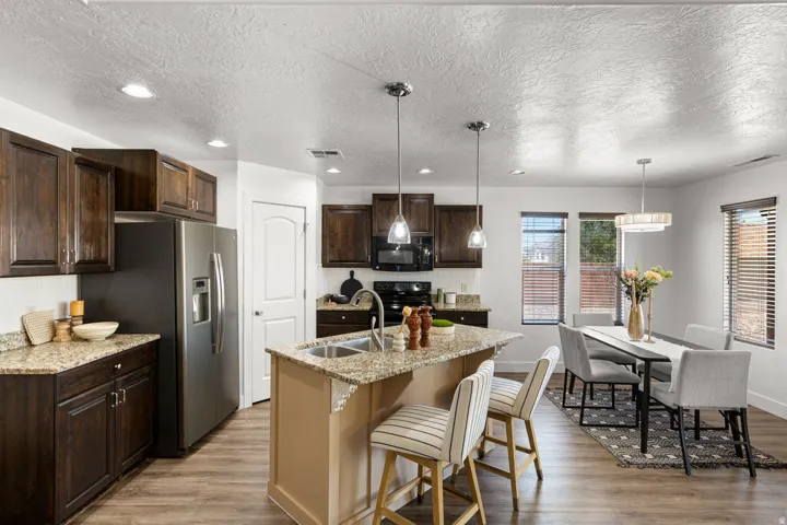 Open-concept kitchen and dining area featuring dark wood cabinetry, granite-finish countertops, stainless steel appliances, and wood-finish flooring