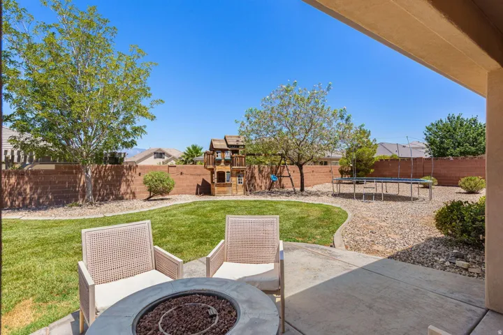 Expansive backyard featuring a concrete patio with a built-in fire pit, manicured lawn, gravel landscaping, and mature trees