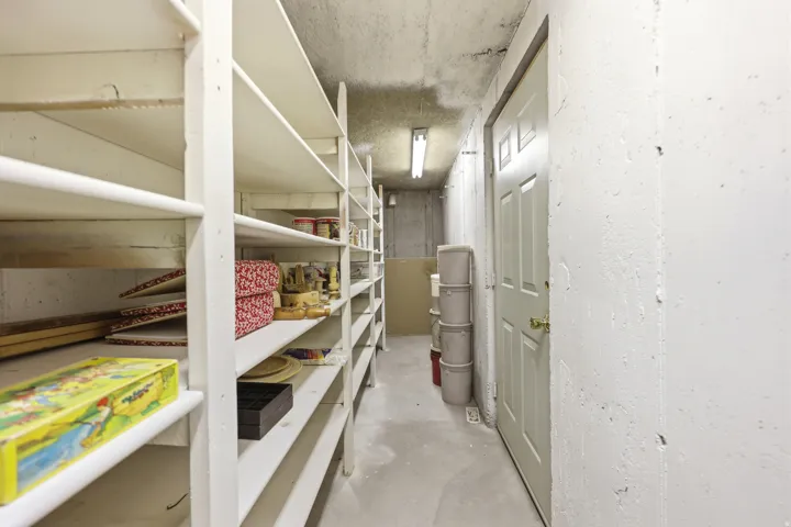 Dedicated storage room featuring extensive built-in shelving, white painted walls, and concrete flooring