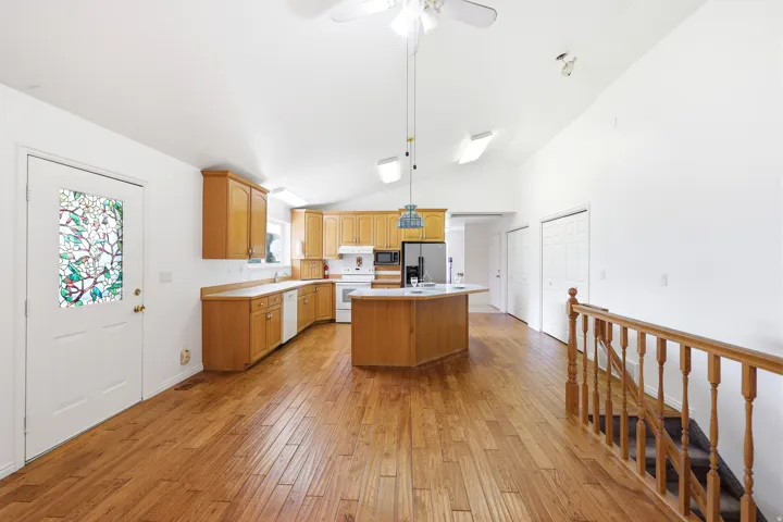 Open-concept living space featuring wood-finish flooring, a kitchen with wood cabinetry and a central island, a stained glass entry door, and a staircase with wood railings