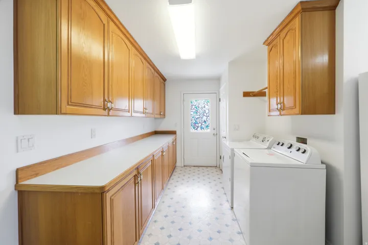 Laundry area featuring extensive wood cabinetry, white countertops, vinyl flooring, and a decorative glass paneled door
