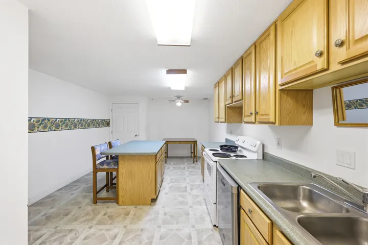 Kitchen featuring wood cabinetry, laminate countertops, a double-basin stainless steel sink, and white appliances