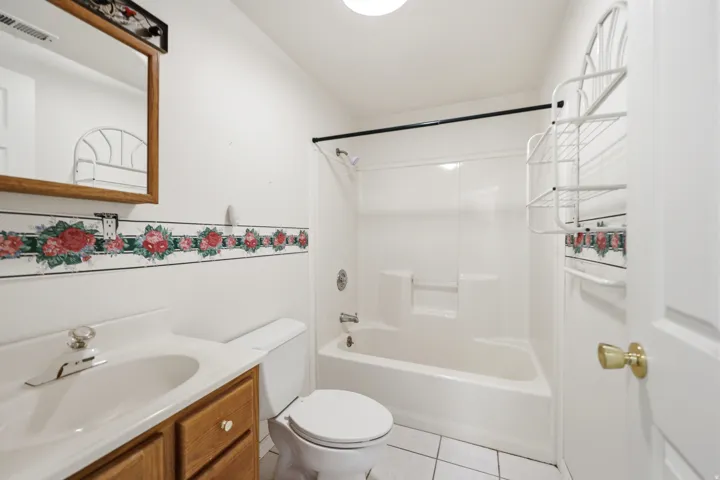Bathroom featuring a white bathtub and shower combination, wood-finish vanity with an integrated sink, white tiled flooring, and a framed mirror
