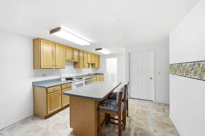 Kitchen featuring light wood cabinetry, laminate countertops, white appliances, and a central island with seating