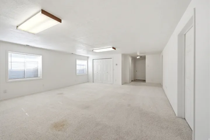 Spacious open room featuring neutral carpeting, abundant natural light from multiple windows, recessed ceiling lighting, and direct access to additional spaces through white interior doors