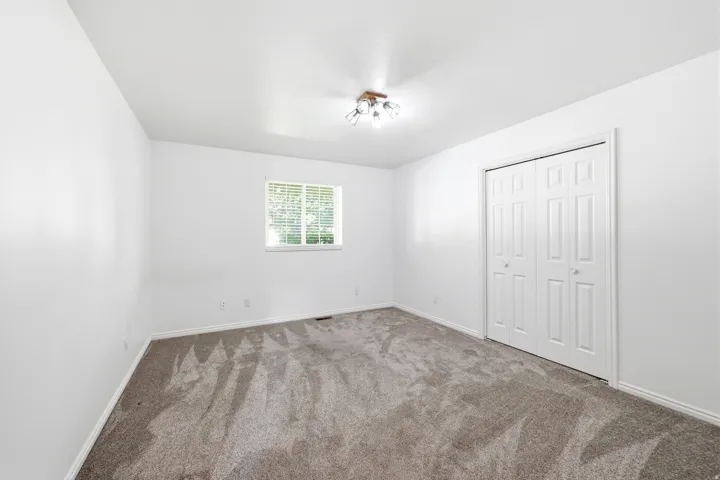 Room with neutral wall paint, gray carpet, a single window with blinds, and a bi-fold closet door