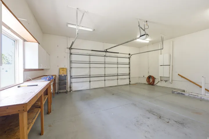 Spacious garage featuring a concrete floor, overhead fluorescent lighting, an automated garage door system, a built-in workbench with storage, and a window for natural light