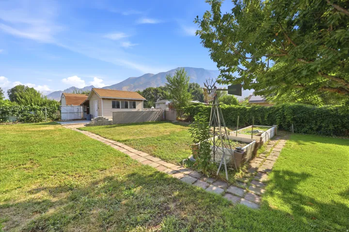 Expansive backyard featuring a stone paver pathway, raised garden beds, a storage shed with an asphalt shingle roof, and distant mountain scenery
