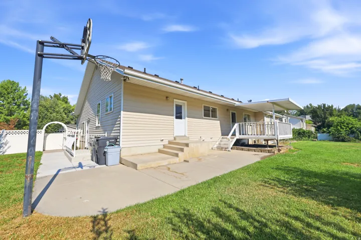 Expansive rear exterior featuring a raised deck with overhead awning, concrete patio, and a basketball hoop