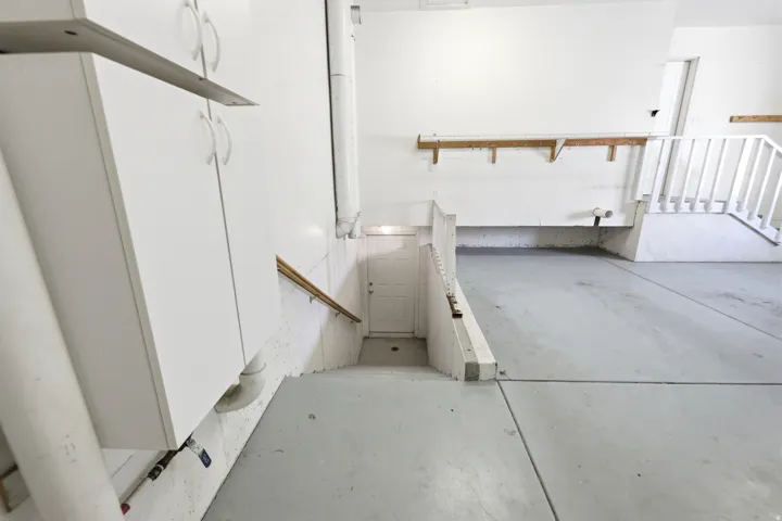 Spacious garage area featuring a concrete floor, built-in white cabinetry, wooden handrail, and an interior access door