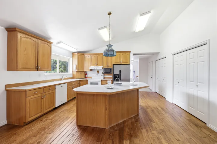 Kitchen featuring wood-finish flooring, light wood cabinetry, a central island with a light-toned countertop, and vaulted ceilings