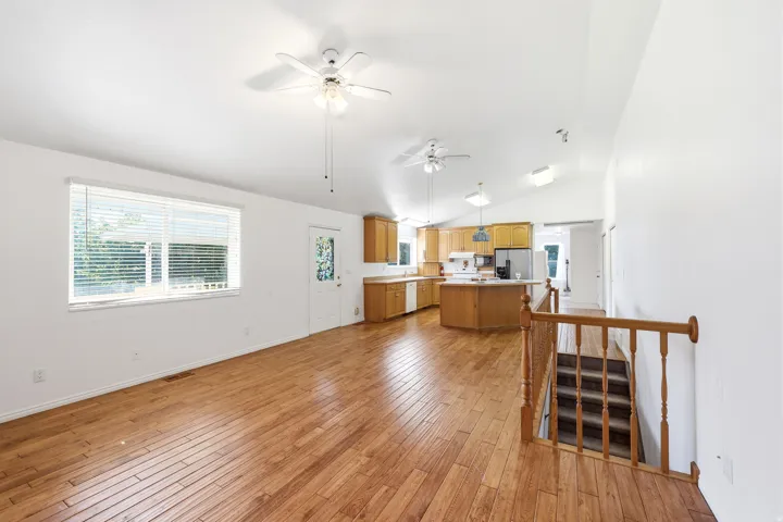Spacious main living area featuring wood-finish flooring, a large window with blinds, and white walls